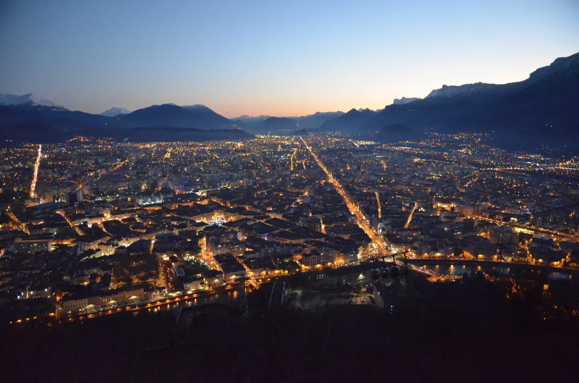 Aerial view of Grenoble at dusk, ringed by the Alps