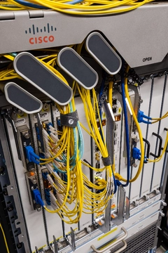 Équipement réseau Cisco avec de multiples fibres jaunes et cyan au sein d'un rack Datacenter